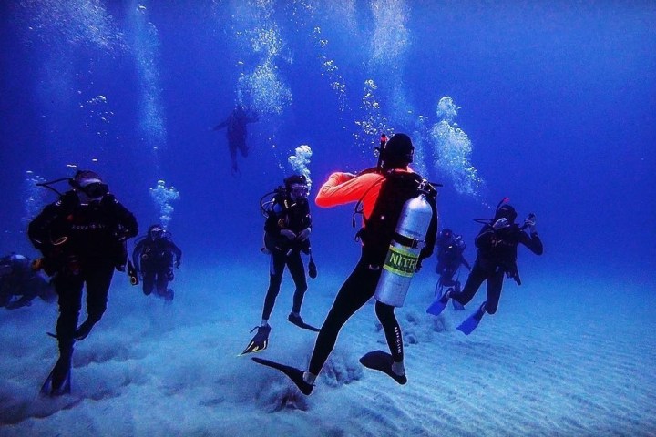 Group of scuba divers underwater with bubbles rising above them.