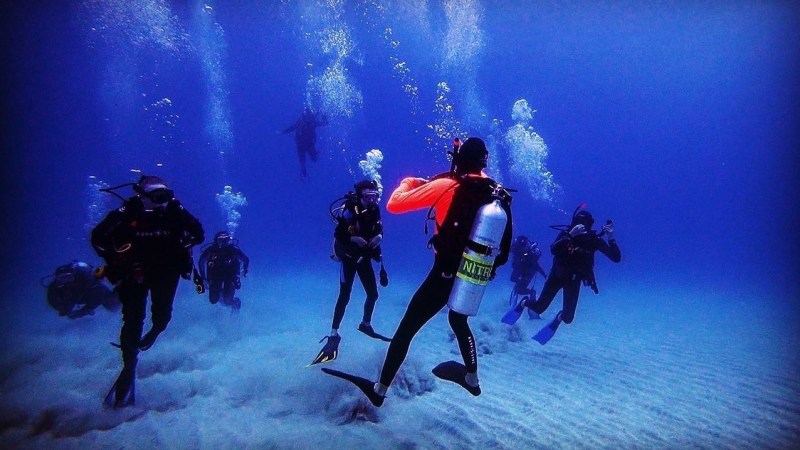 Group of scuba divers underwater with bubbles rising above them.
