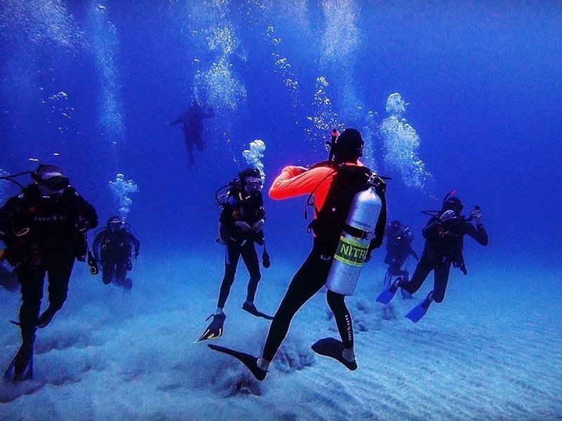 Group of scuba divers underwater with bubbles rising above them.
