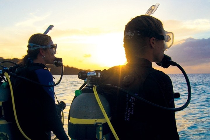 Two scuba divers in wetsuits watch sunset over ocean.