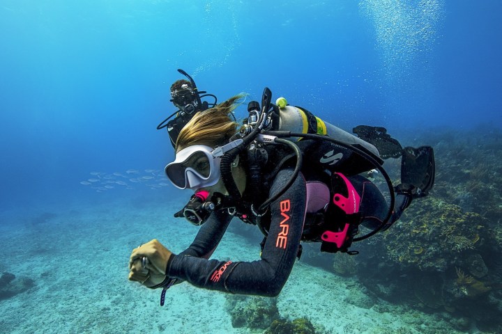 Scuba diver in black and pink gear swimming underwater near coral reef.