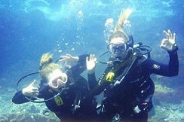 Two scuba divers underwater making OK signs in a clear ocean.