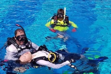 Scuba divers practicing rescue techniques in a swimming pool.