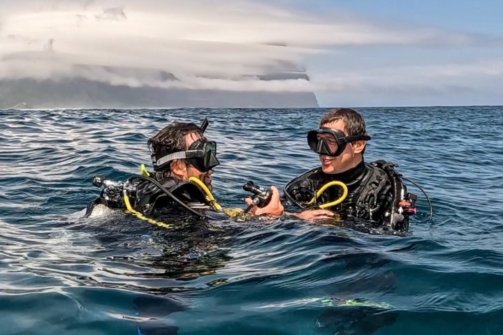 Two scuba divers in the ocean, with a cloud-covered mountain in the background.