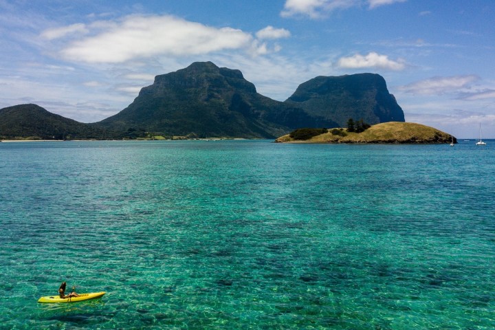 Person kayaking on clear turquoise water with mountains and islands in the background.