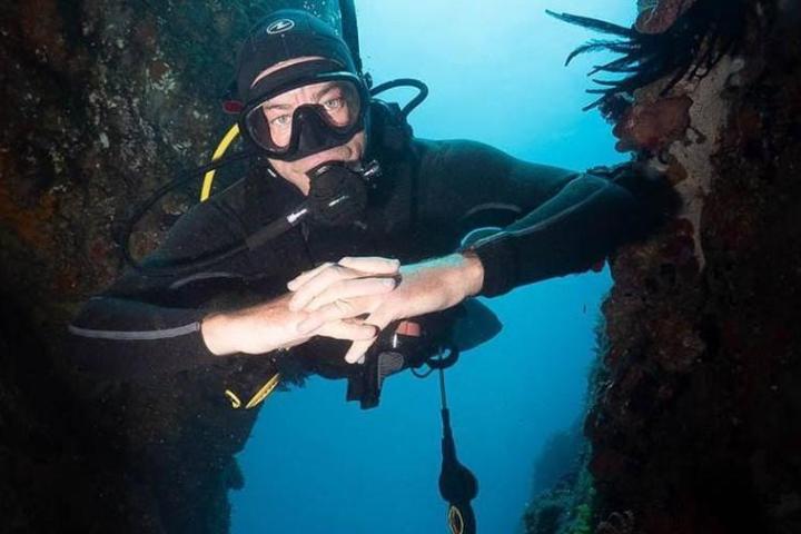 Scuba diver in wetsuit exploring underwater cave with rocks on both sides.