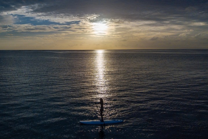 Person paddleboarding on calm ocean at sunset with a reflective sky.