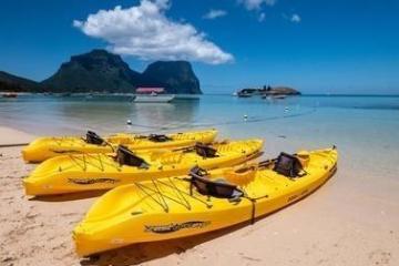 Four yellow kayaks on a sandy beach with turquoise water and mountains in the background.