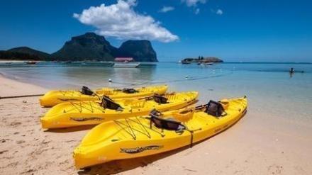 Four yellow kayaks on a sandy beach with turquoise water and mountains in the background.