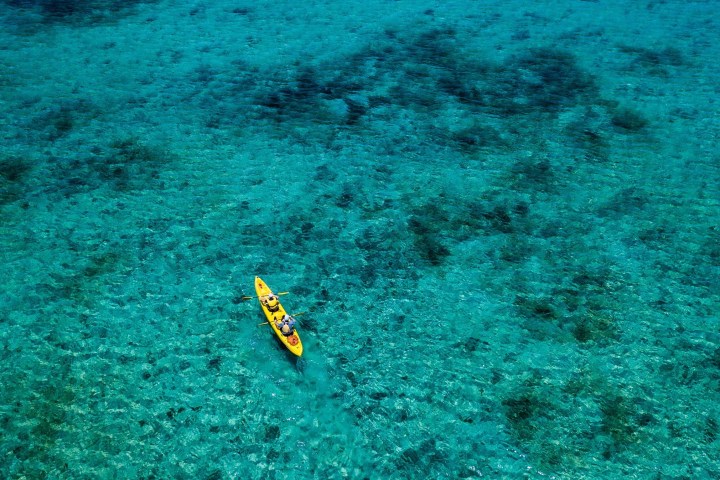 Two people kayaking in clear turquoise water, aerial view.