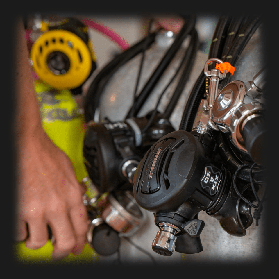 imgi_4_ Close-up of dive equipment with a focus on a regulator and hand.